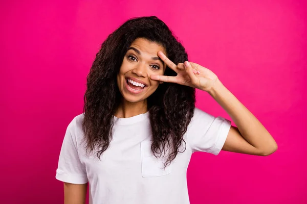 Photo de joyeuse brune bouclée jeune femme montrer v-signe usure blanc t-shirt isolé sur fond rose vif de couleur — Photo