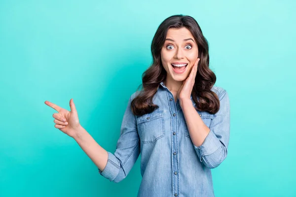 Foto de mujer conmocionada dulce usar jeans camisa brazo mejilla señalando el dedo espacio vacío sonriendo aislado color turquesa fondo —  Fotos de Stock