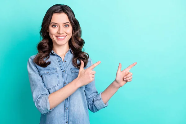 Foto di impressionato dolce giovane donna indossare jeans camicia puntando due dita spazio vuoto sorridente isolato sfondo di colore turchese — Foto Stock