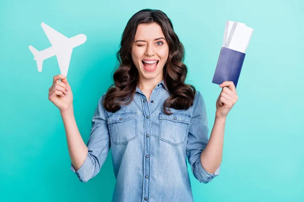 Foto de menina feliz sorriso positivo piscar olho avião voar no exterior bilhetes de férias passaporte isolado sobre fundo cor teal — Fotografia de Stock