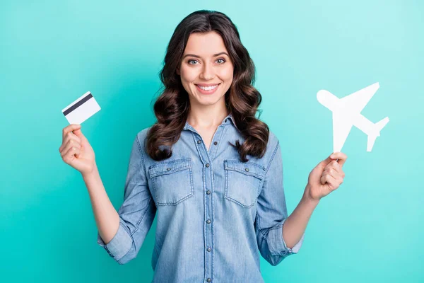 Foto de impressionado brilhante jovem mulher usar jeans camisa segurando papel avião cartão de crédito sorrindo isolado cor turquesa fundo — Fotografia de Stock