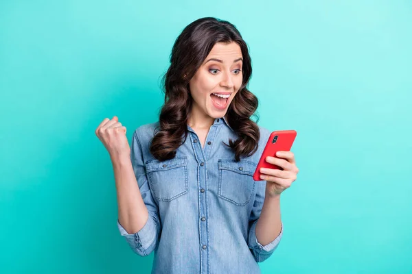 Foto de muito doce jovem senhora vestida camisa jeans sorrindo olhando gadget moderno levantando punho isolado cor teal fundo — Fotografia de Stock
