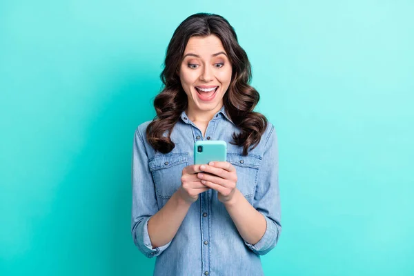 Photo funky excité jeune femme habillée chemise en denim souriant bavarder gadget moderne isolé fond de couleur sarcelle — Photo