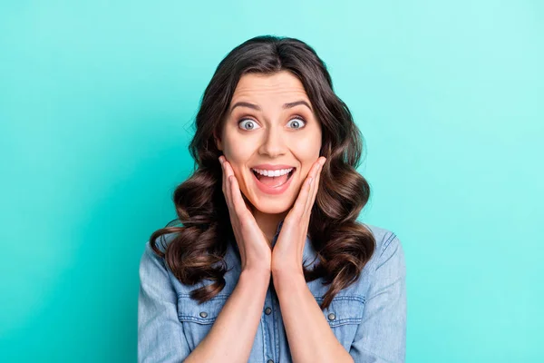 Foto de mujer joven sorprendida difícil de usar jeans camisa brazos mejillas boca abierta sonriendo aislado color turquesa fondo — Foto de Stock