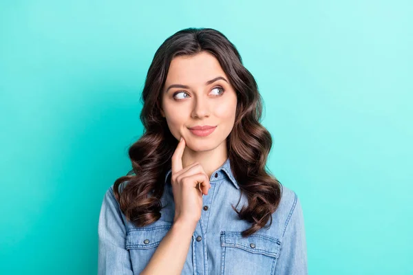 Foto de mujer joven divertida y difícil de usar jeans camisa dedo mejilla buscando espacio vacío sonriendo aislado color turquesa fondo —  Fotos de Stock