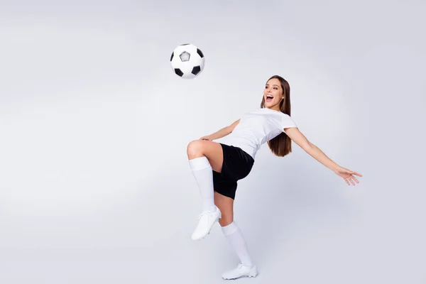 Foto de cuerpo completo de mujer emocionada jugador equipo de fútbol patada pierna control bola mostrando trucos de estilo libre usar fútbol uniforme camiseta pantalones cortos botas rodilla calcetines aislados color blanco fondo — Foto de Stock