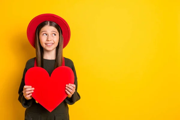 Foto retrato de menina linda mantendo coração vermelho em forma de cartão postal olhando copyspace isolado vibrante cor amarela fundo — Fotografia de Stock