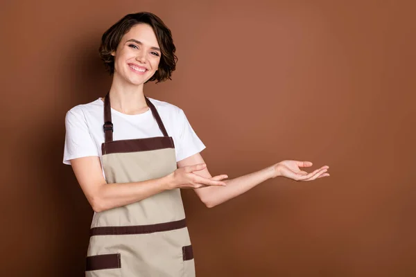 Retrato de atraente alegre menina alegre barista café demonstrando espaço de cópia bem-vindo isolado sobre fundo de cor marrom — Fotografia de Stock