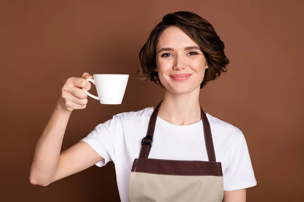 Retrato de menina alegre atraente barista segurando em mãos trazendo café expresso bom gosto aroma isolado sobre fundo de cor marrom — Fotografia de Stock