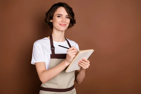 Foto di affascinante giovane ragazza braccia tenere penna notebook guarda fotocamera hanno buon umore isolato su sfondo di colore marrone — Foto Stock