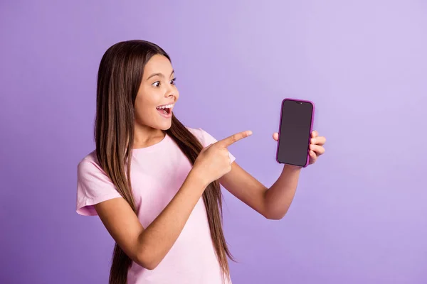 Foto de niña bastante emocionada usar camiseta rosa buscando apuntando moderno gadget espacio vacío aislado color violeta fondo — Foto de Stock