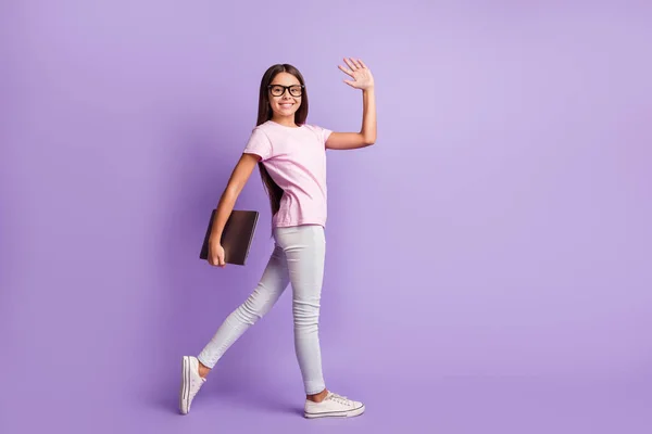 Foto de bonito estudante bonita vestida rosa t-shirt andando segurando dispositivo moderno acenando braço isolado cor roxa fundo — Fotografia de Stock