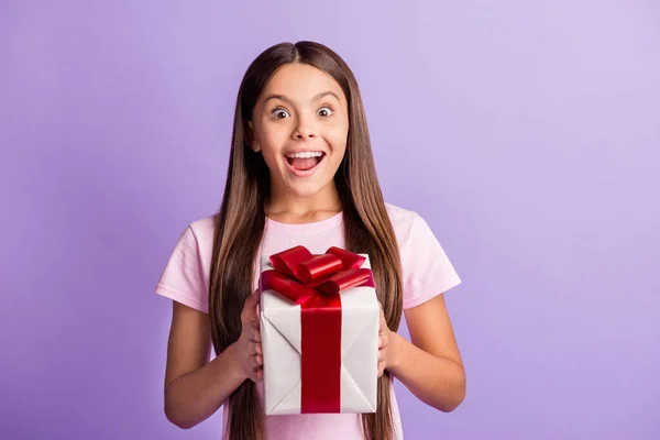 Foto de divertida niña emocionada usar camiseta rosa consiguiendo caja de regalo de cumpleaños aislado color violeta fondo — Foto de Stock