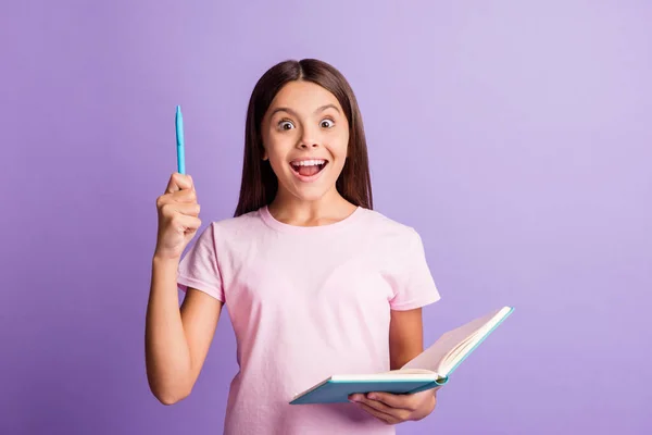 Foto av geni rolig skolflicka klädd rosa t-shirt pekar penna tomt utrymme håller copybook isolerad lila färg bakgrund — Stockfoto