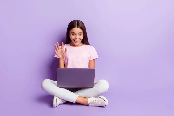 Foto von glänzenden süßen Mädchen tragen rosa T-Shirt Sitzboden mit Videoanruf modernes Gadget winkenden Arm isoliert violette Farbe Hintergrund — Stockfoto