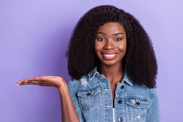 Φωτογραφία του ευτυχισμένη καλή διάθεση όμορφη αφρικανή γυναίκα κατέχουν χέρι διαφημιστικό προϊόν που απομονώνονται σε μωβ φόντο χρώμα — Φωτογραφία Αρχείου