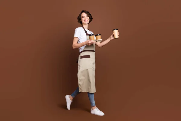 Ganzkörpergröße Ansicht der attraktiven fröhlichen Mädchen bringen Kaffee serviert isoliert über braunen Farbhintergrund — Stockfoto