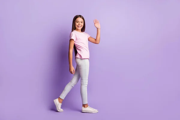Zdjęcie uroczej młodej dziewczyny nosić różowy t-shirt machając ramię chodzenie odizolowane fioletowy kolor tła — Zdjęcie stockowe