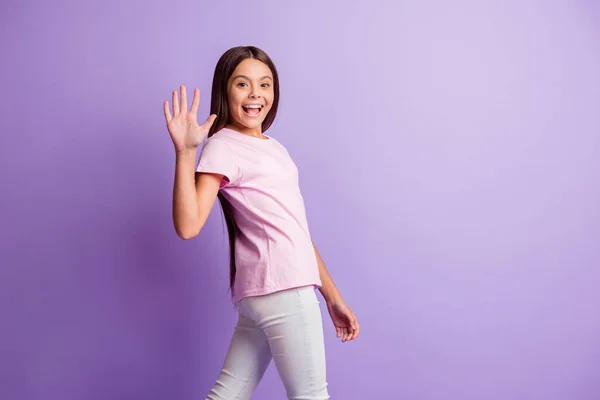 Foto de encantadora colegiala dulce vestida camiseta rosa caminando brazo de agitación aislado color púrpura fondo — Foto de Stock