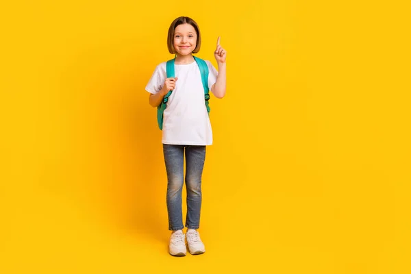 Volledige lengte body size foto schoolmeisje glimlachend dragen van blauwe rugzak wijzen omhoog copyspace geïsoleerde levendige gele kleur achtergrond — Stockfoto