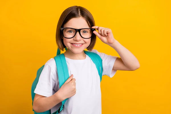 Foto ritratto piccola studentessa sorridente indossare occhiali blu zaino isolato vibrante colore giallo sfondo — Foto Stock