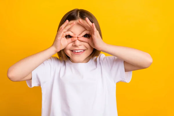 Foto ritratto piccola studentessa sorridente giocoso tenere le mani come binocolo guardare isolato vibrante colore giallo sfondo — Foto Stock