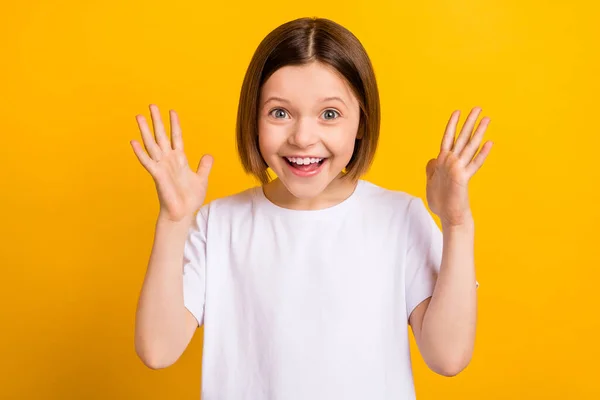 Foto von niedlichen beeindruckt Schulmädchen gekleidet weißen Outfit steigende Arme lächelnd isoliert gelbe Farbe Hintergrund — Stockfoto