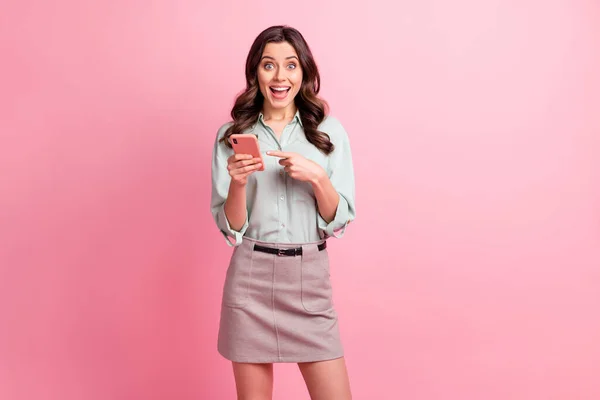 Foto de chocado surpreendido jovem mulher apontar notificação de telefone dedo isolado no fundo cor-de-rosa — Fotografia de Stock