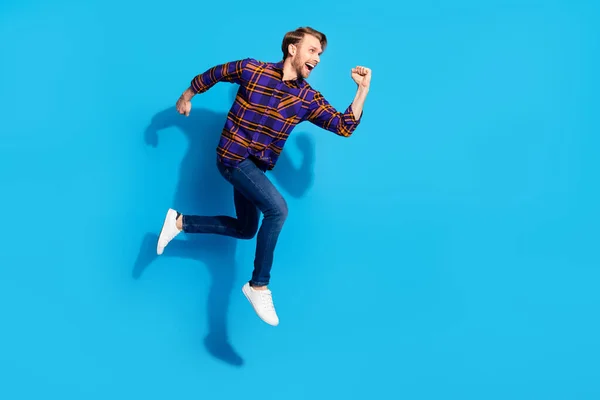 Фото фанки спешащего молодого джентльмена в клетчатой рубашке, улыбающегося прыгая на изолированном голубом фоне — стоковое фото