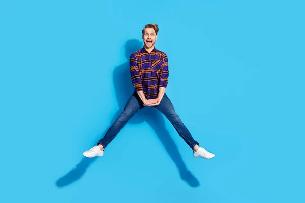 Foto av söt funky ung gentleman klädd rutig skjorta ler hoppa högt isolerad blå färg bakgrund — Stockfoto