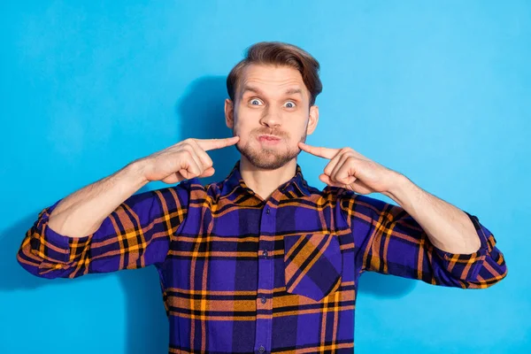 Portrait of satisfied young person holding breath fingers on cheeks isolated on blue color background