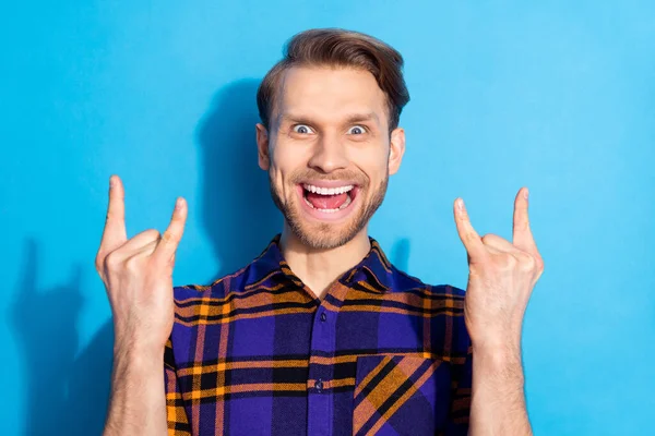 Photo of cheerful happy crazy young man make horned signs good mood rock isolated on blue color background — Stock Photo, Image