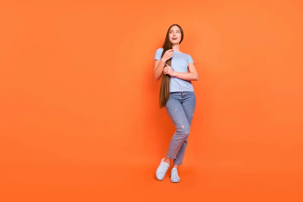 Foto de tamaño completo de la joven adolescente feliz sonrisa positiva manos tacto pelo mirada espacio vacío aislado sobre fondo de color naranja — Foto de Stock