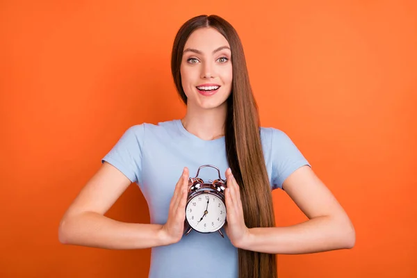 Foto de otimista milenar longo penteado senhora segurar relógio desgaste azul t-shirt isolado no fundo cor de laranja — Fotografia de Stock