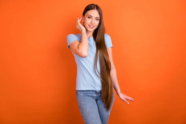 Foto de lindo millennial lady touch pelo desgaste azul camiseta vaqueros aislados en fondo de color naranja — Foto de Stock