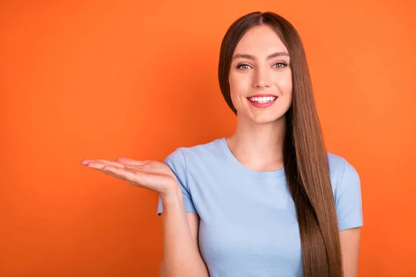 Foto de bastante largo peinado millennial lady hold espacio vacío desgaste azul camiseta aislada sobre fondo de color naranja — Foto de Stock