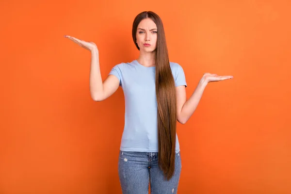 Foto de incerto longo penteado milenar senhora segurar espaço vazio acho que usar camiseta azul isolado no fundo cor de laranja — Fotografia de Stock