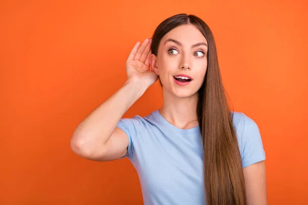 Foto de peinado marrón impresionado joven dama oreja mirada espacio vacío desgaste camiseta azul aislado en fondo de color naranja vivo —  Fotos de Stock