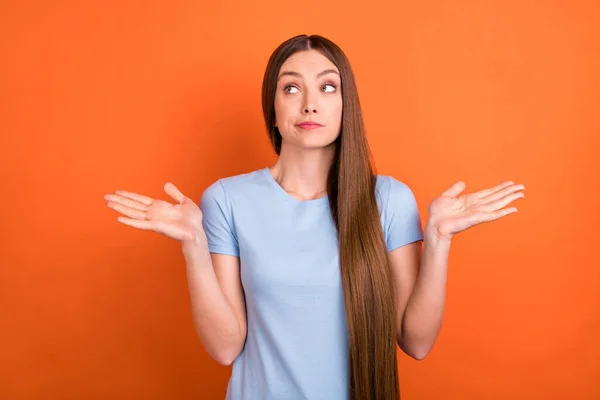 Foto von unsicheren braunen Frisur junge Dame achselzuckend aussehen leeren Raum tragen blaues T-Shirt isoliert auf lebhaften orangefarbenen Hintergrund — Stockfoto