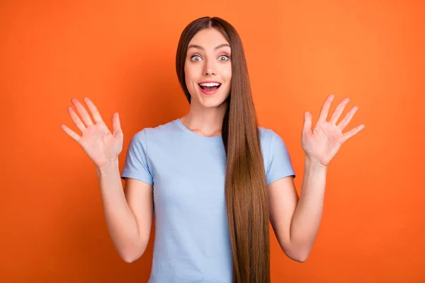 Foto de impressionado longo penteado jovem senhora mãos para cima desgaste azul t-shirt isolado no fundo de cor laranja vívida — Fotografia de Stock