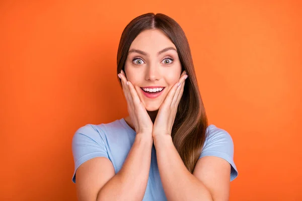 Foto del peinado marrón impresionado millennial lady manos cara desgaste camiseta azul aislado sobre fondo de color naranja vivo — Foto de Stock