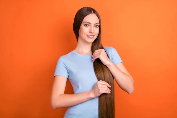 Фото оптимистичного длинные волосы молодая леди прикосновения волосы носить голубую футболку изолированы на ярком оранжевом фоне — стоковое фото
