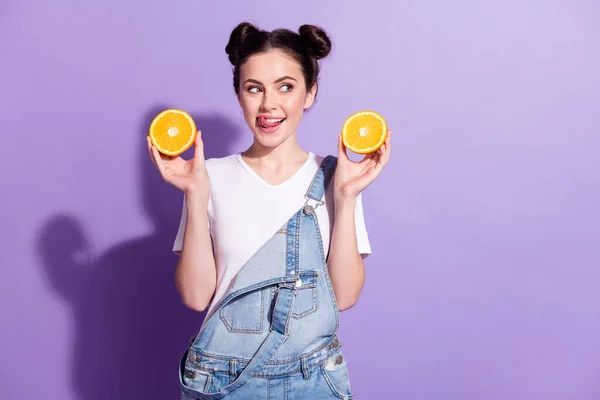 Çekici bir kızın fotoğrafı dişlerini yalıyor. Lezzetli meyve portakallı yiyecekler menekşe rengi arka planda izole edilmiş. — Stok fotoğraf