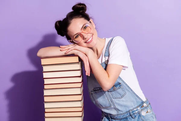 Portrait of pretty positive young girl hands head on book stack beaming smile isolated on purple color background — Stock Photo, Image