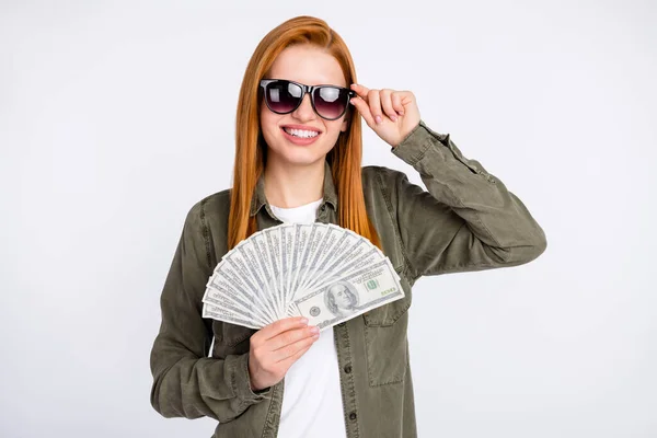 Foto de alegre bonito cabelo vermelho senhora toque óculos segurar dinheiro desgaste camisa cinza isolado no fundo de cor branca — Fotografia de Stock