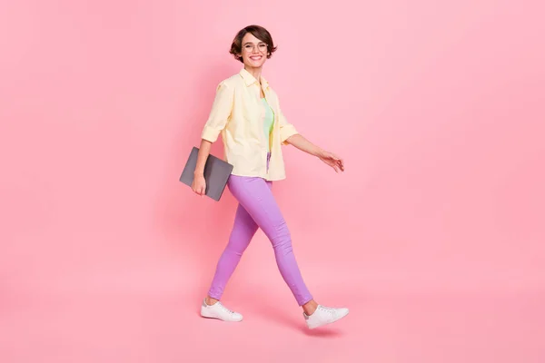 可愛いです若い女性の服を着た黄色のシャツ眼鏡歩く開催近代的なガジェット隔離されたピンク色の背景 — ストック写真