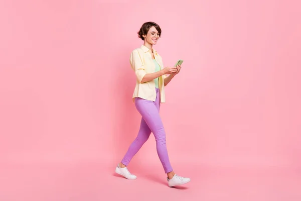 Foto van charmante jonge dame gekleed geel shirt bril lopen typen moderne gadget geïsoleerde roze kleur achtergrond — Stockfoto
