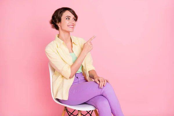 Foto van opgewonden mooie jonge vrouw dragen geel shirt zit stoel wijzen lege ruimte geïsoleerde roze kleur achtergrond — Stockfoto