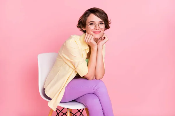 Fénykép aranyos csinos fiatal hölgy öltözött sárga ing szemüveg ül szék karok arc elszigetelt rózsaszín szín háttér — Stock Fotó