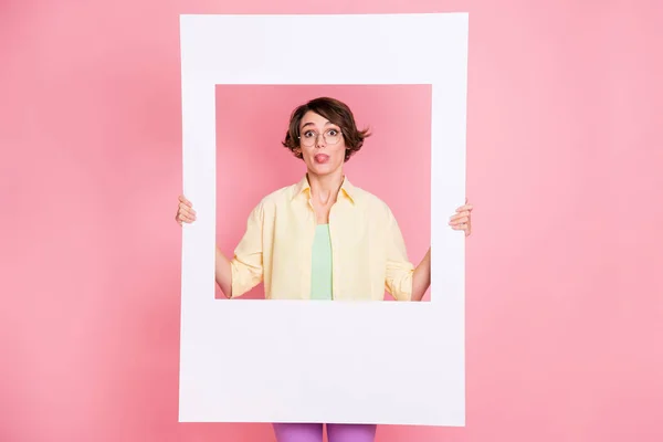 Foto de mujer morena optimista sostener marco mostrar lengua usar camisa aislada sobre fondo de color rosa pastel — Foto de Stock